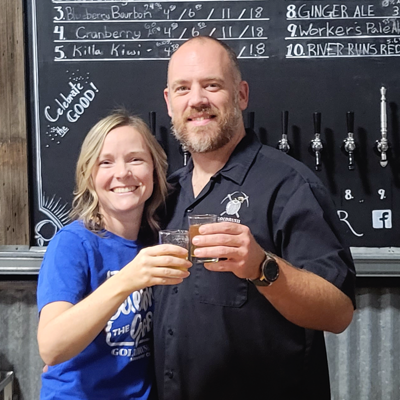 Founders Holly and Sid Dyer stand together behind the bar, holding glasses of cider.